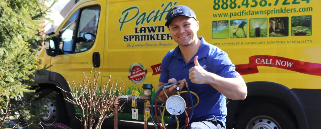 A smiling Pacific Lawn Sprinkler technician gives a thumbs up while holding equipment in front of