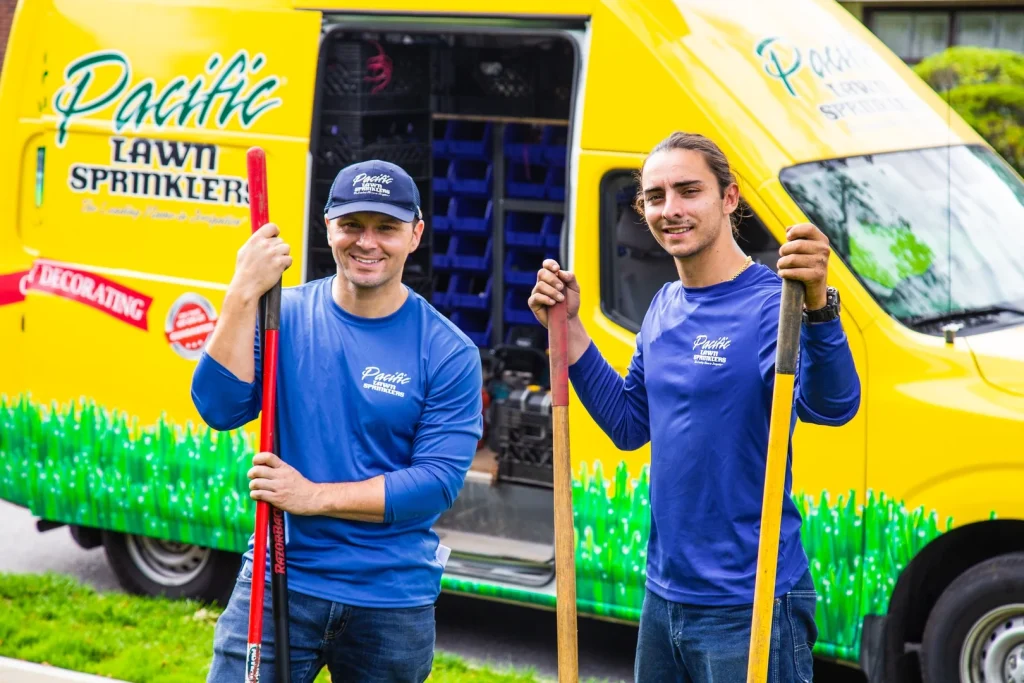 Two smiling Pacific Lawn Sprinklers technicians hold tools in front of their branded yellow service van